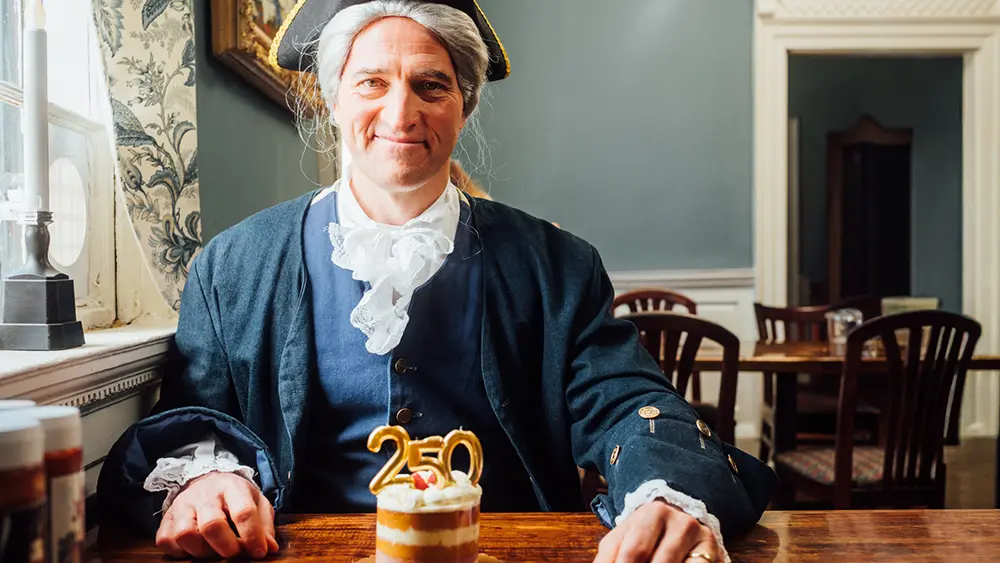 George Washington re-enactor enjoying a cake with candles in the shape of 250
