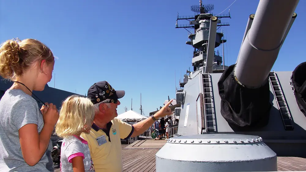 Older gentleman showing two children the guns on a Navy battleship.